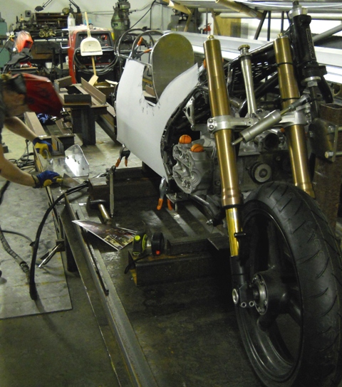 FABRICATOR CHRIS WORKING ON A GAS TANK WHILE I LAY OUT MOCK UP FOR ALUMINUM PANELS FOR SIDES OF BIKE